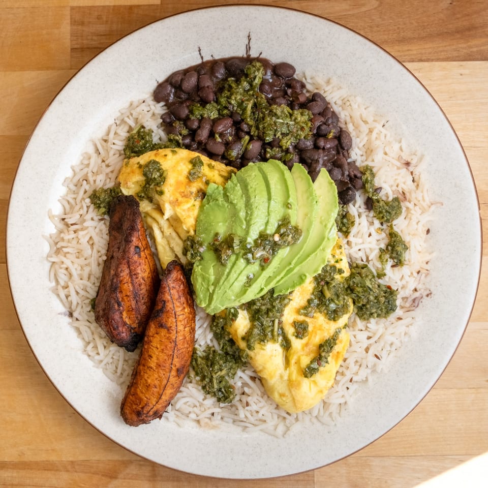 B'Gabs healthy plate with rice, black beans, omelet, avocado, and plantains, drizzled with green sauce.