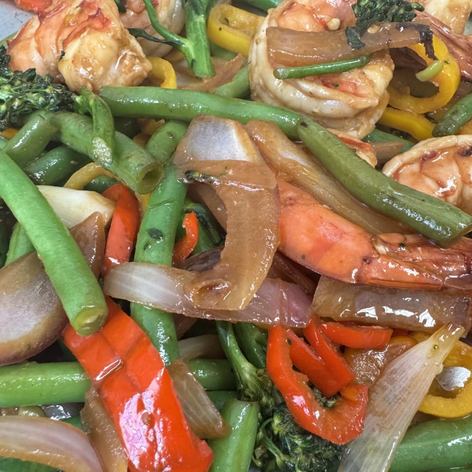Close-up of shrimp stir-fry with green beans, broccoli, red and yellow bell peppers, and onions.