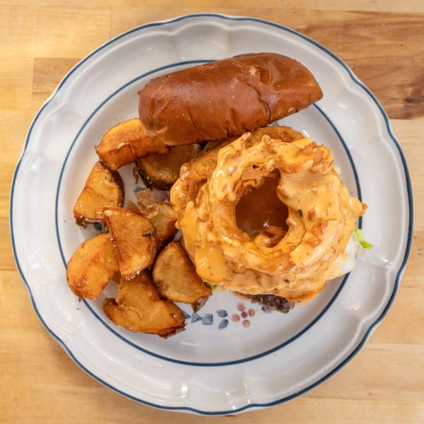 A burger with a large onion ring and special sauce, served with potato wedges on a white plate.