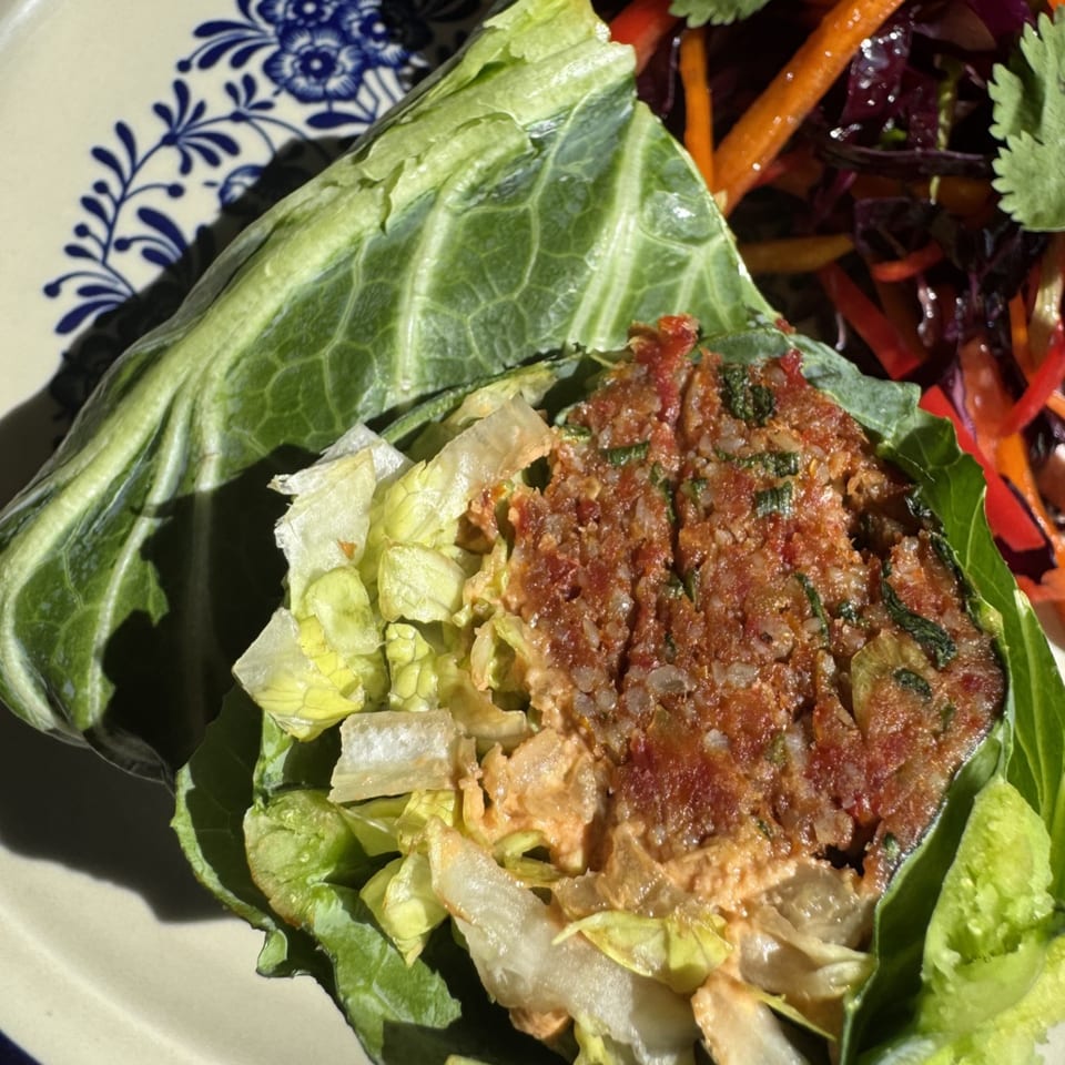 Close-up of a collard green wrap filled with ground meat, rice, and lettuce, served with a side salad.