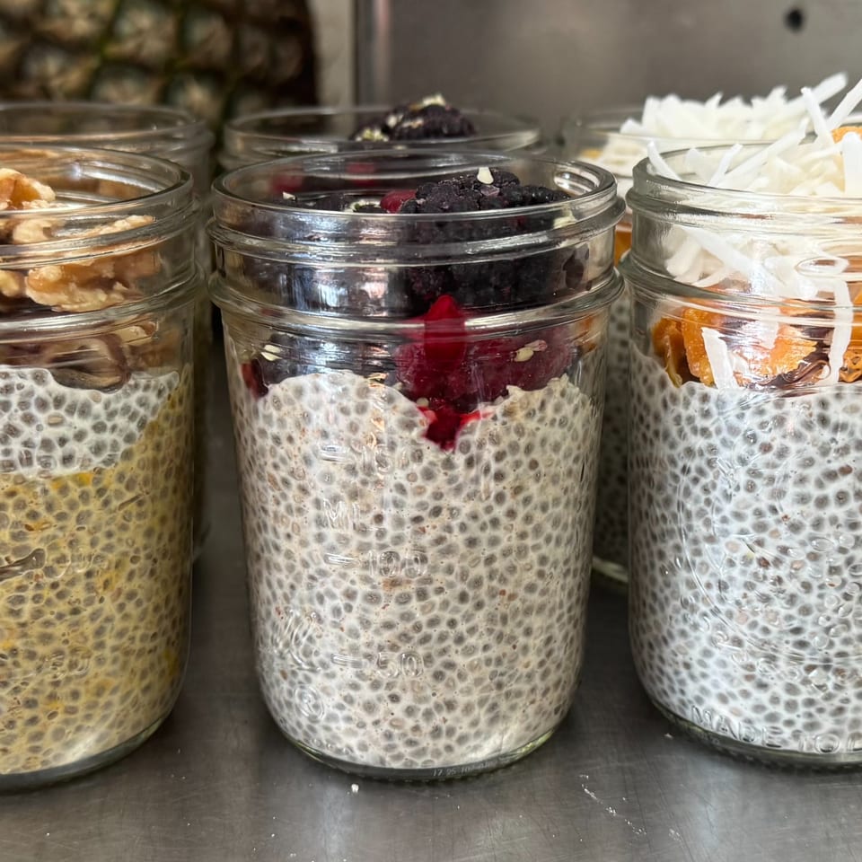 Three glass jars of chia seed pudding, topped with walnuts, berries, and shredded coconut.