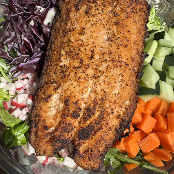 Close-up of a seasoned fish fillet with red cabbage, radishes, cucumbers, and carrots.