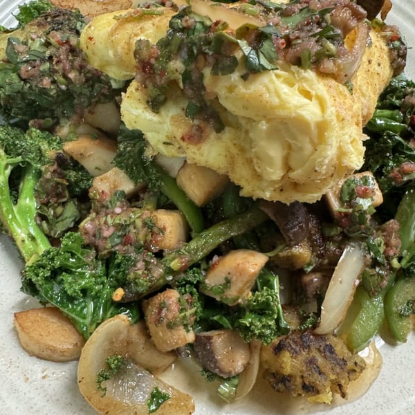 Close-up of a dish with scrambled eggs, kale, mushrooms, and onions, topped with a savory sauce.