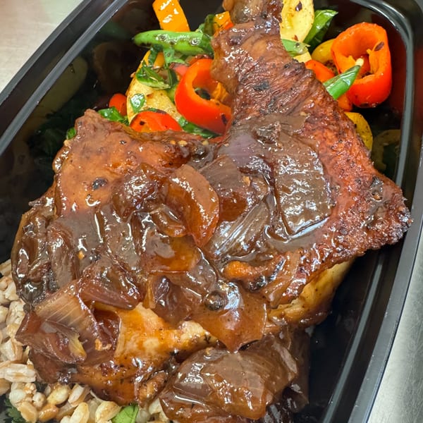 Close-up of a chicken thigh with onions and sauce, served with roasted vegetables and grains.