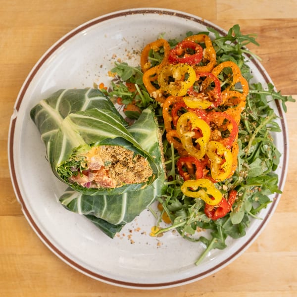 A healthy collard green wrap with a side of arugula and colorful bell peppers on a white plate.