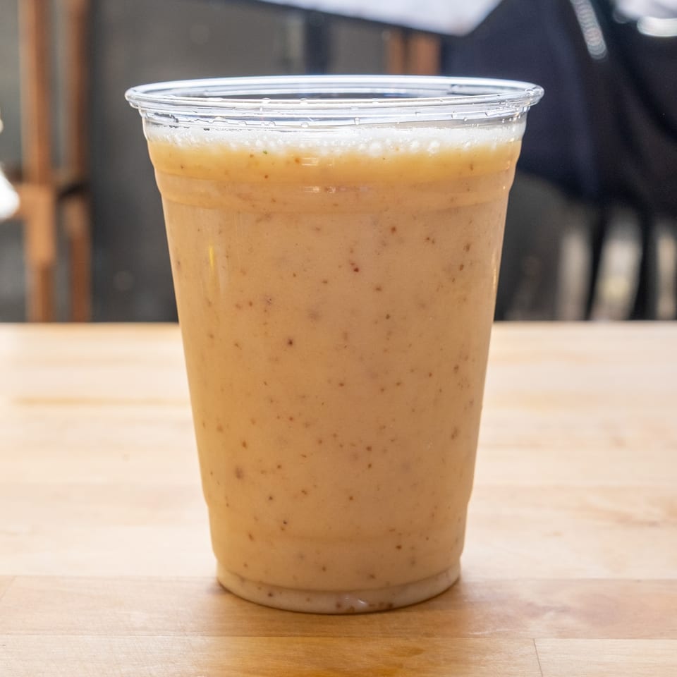 A B'Gabs Comfort Cafe healthy smoothie in a clear plastic cup on a wooden table.