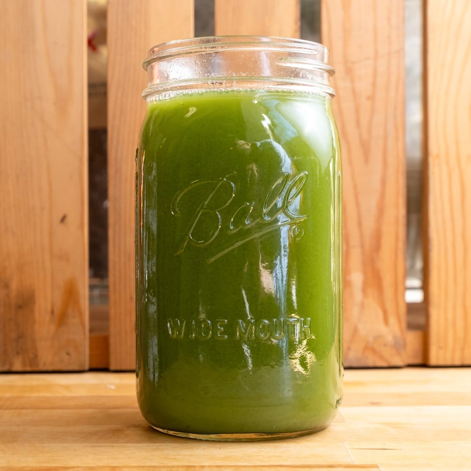 A Ball Wide Mouth mason jar filled with bright green juice sits on a wooden surface.