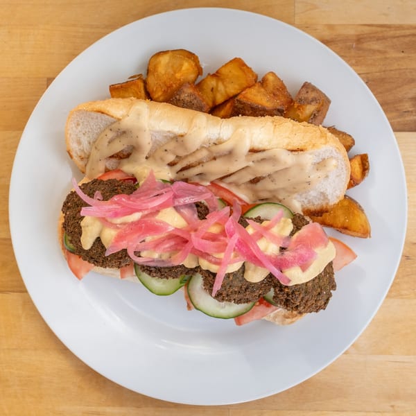 B'Gabs falafel sandwich with pickled onions, cucumbers, tomatoes, and sauce, served with potato wedges.