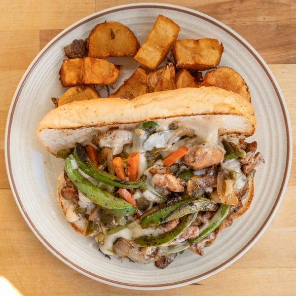 A B'Gabs Comfort Cafe chicken cheesesteak with peppers, onions, and mushrooms, served with potato wedges.