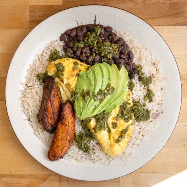 A healthy B'Gabs meal with rice, black beans, omelet, avocado slices, and plantains, topped with green sauce.