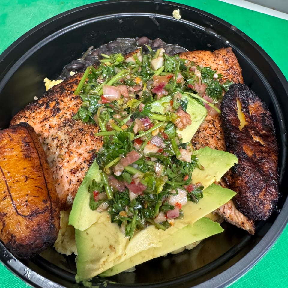 Salmon with avocado, salsa, plantains, and black beans in a black bowl.