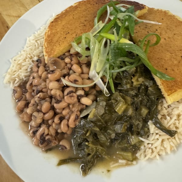 A plate of black-eyed peas, collard greens, rice, and two pieces of cornbread, garnished with scallions.