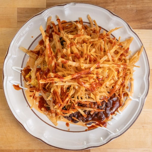 A plate of B'Gabs Comfort Cafe's healthy nachos, topped with black beans, sauce, and crispy fried strips.